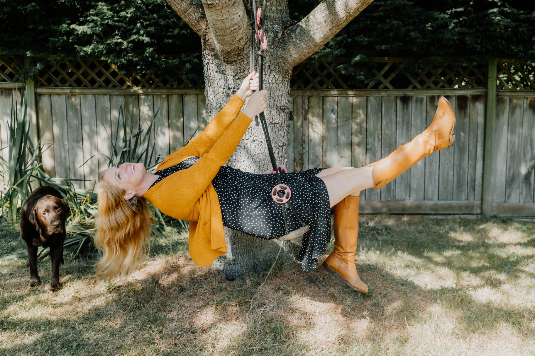 Erin Beattie, founder of Nila, laughing on a tree swing in a sunlit backyard with her chocolate Labrador nearby.